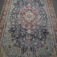 Close up of distressed Persian rug showing intricate floral medallion with red and ivory motifs