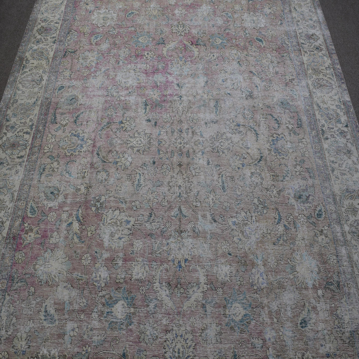 Close up of distressed Persian rug showing faded floral motifs on ivory background