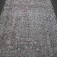 Close up of distressed Persian rug showing faded floral motifs on ivory background