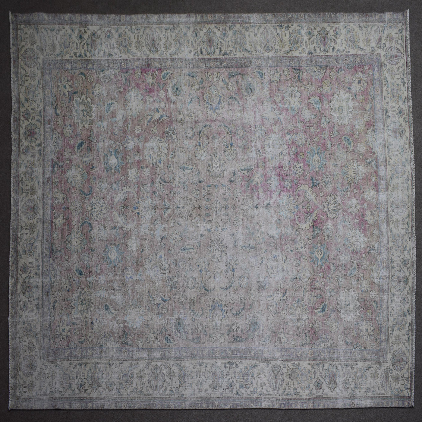Hand knotted Persian rug photographed at an angle showing overall distressed pattern and neutral color palette