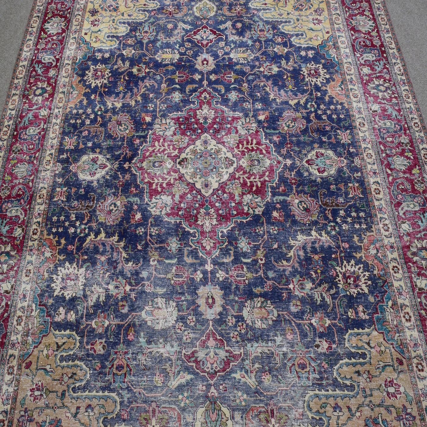 Close up of distressed Persian rug showing intricate medallion with red and ivory floral motifs