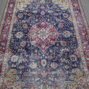 Close up of distressed Persian rug showing intricate medallion with red and ivory floral motifs