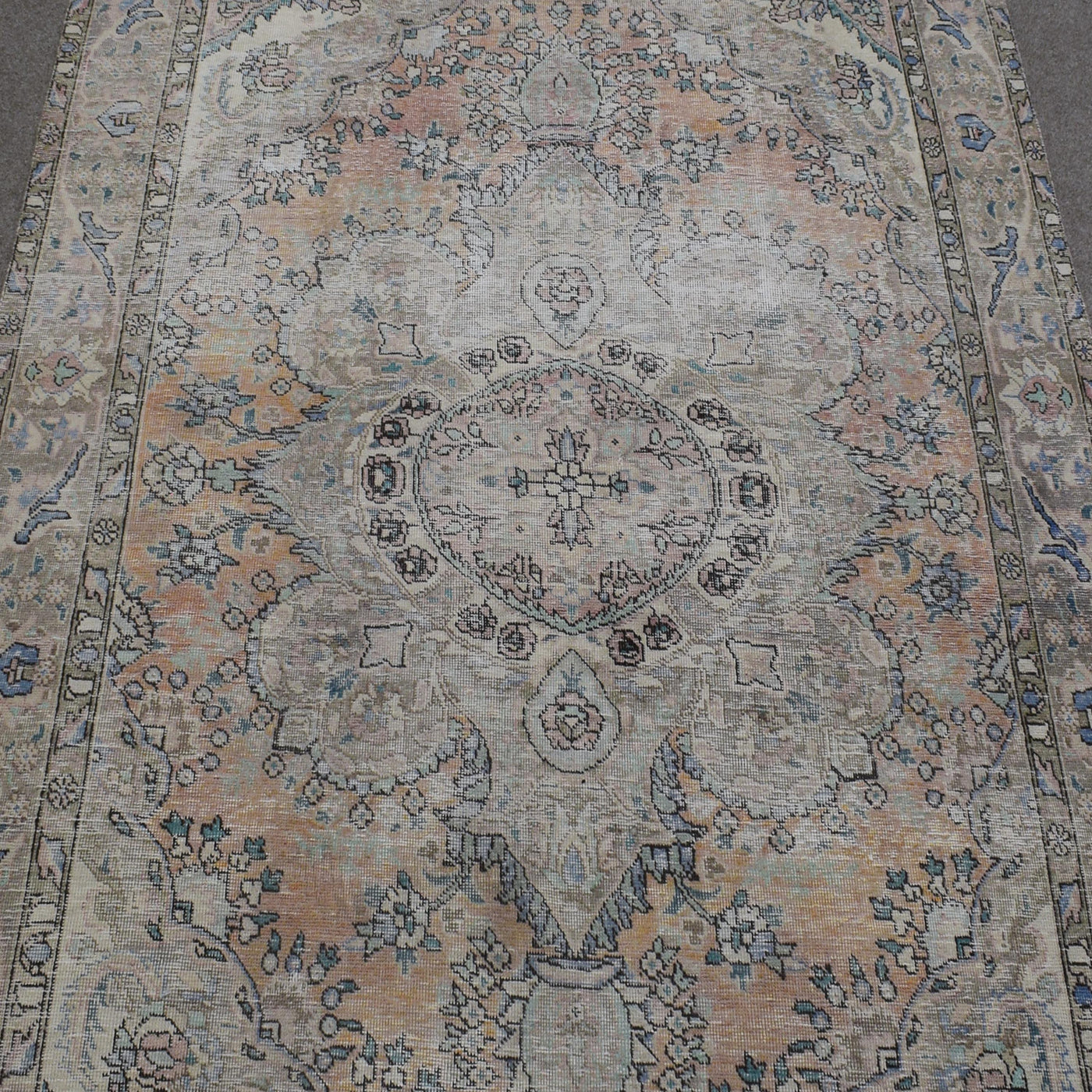Close up of distressed Persian rug showing intricate oval medallion with subtle blue and beige motifs