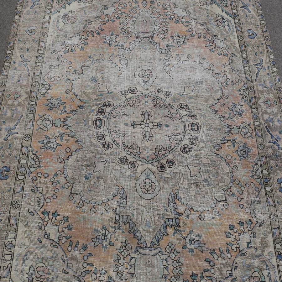 Close up of distressed Persian rug showing intricate oval medallion with subtle blue and beige motifs