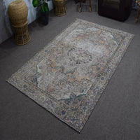 Hand knotted Persian rug photographed at an angle showing overall medallion layout and distressed neutral palette