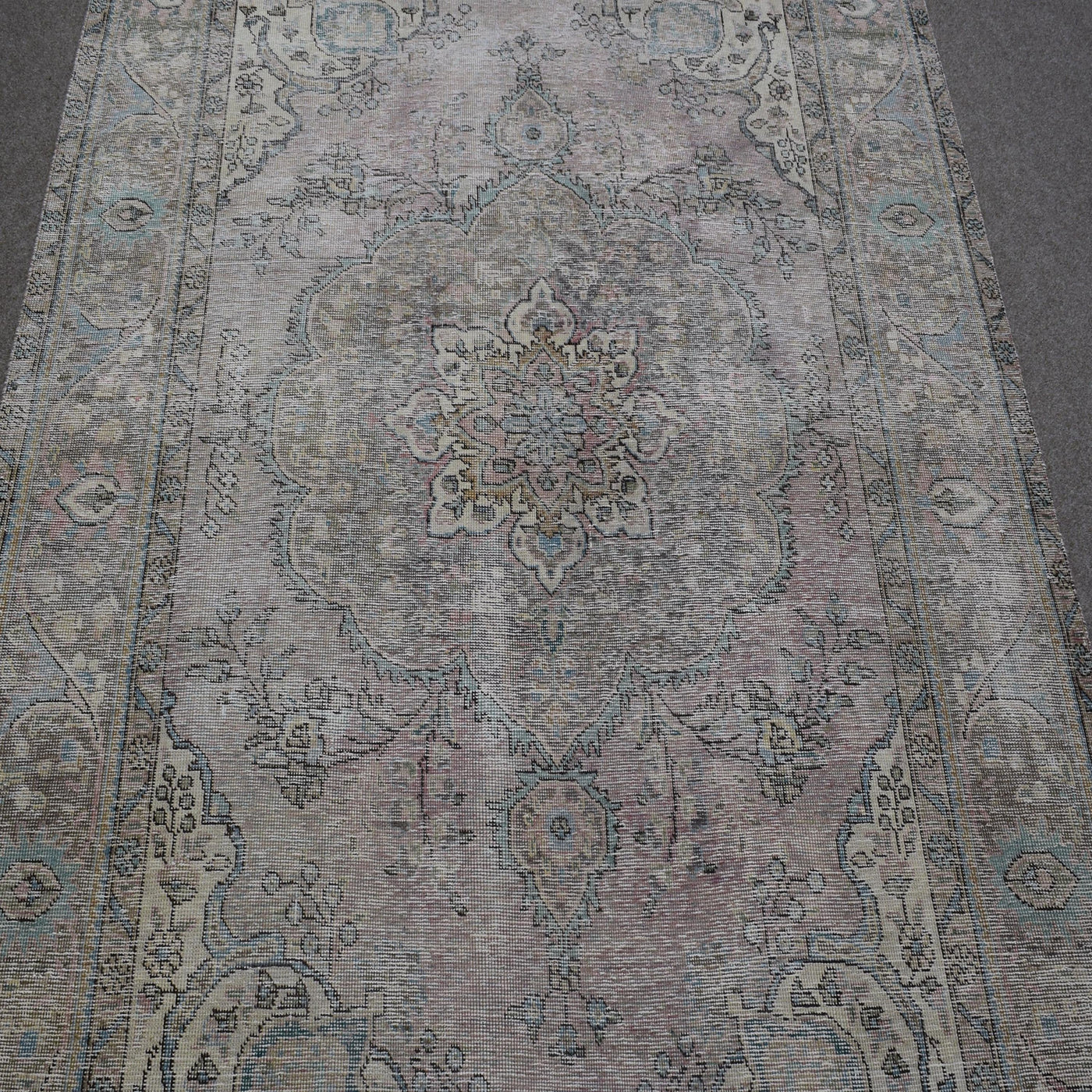 Close up of distressed Persian rug showing faded medallion with delicate floral motifs