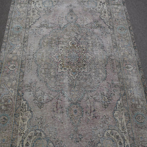 Close up of distressed Persian rug showing faded medallion with delicate floral motifs