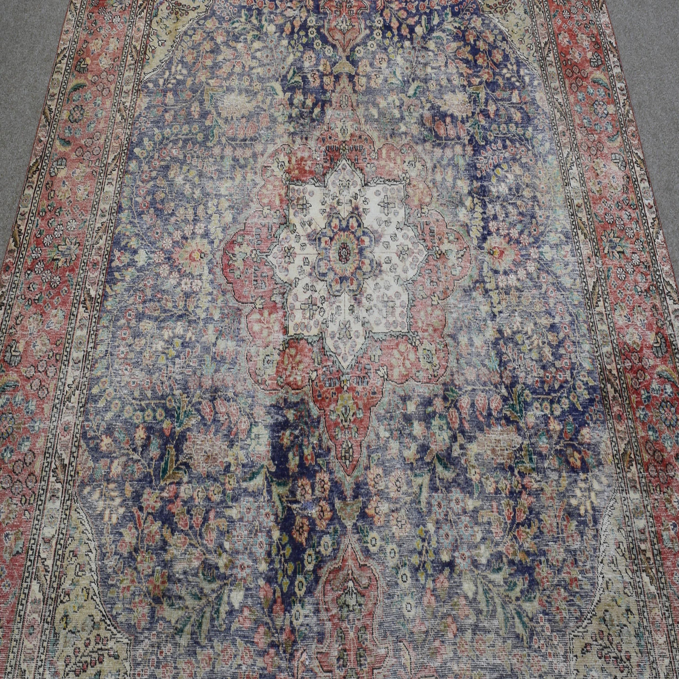 Close up of distressed Persian rug showing intricate central medallion with ivory and red floral motifs