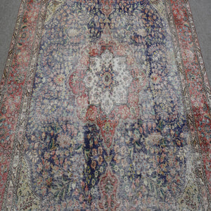 Close up of distressed Persian rug showing intricate central medallion with ivory and red floral motifs