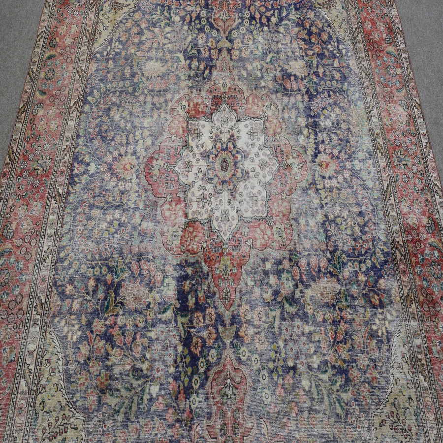 Close up of distressed Persian rug showing intricate central medallion with ivory and red floral motifs