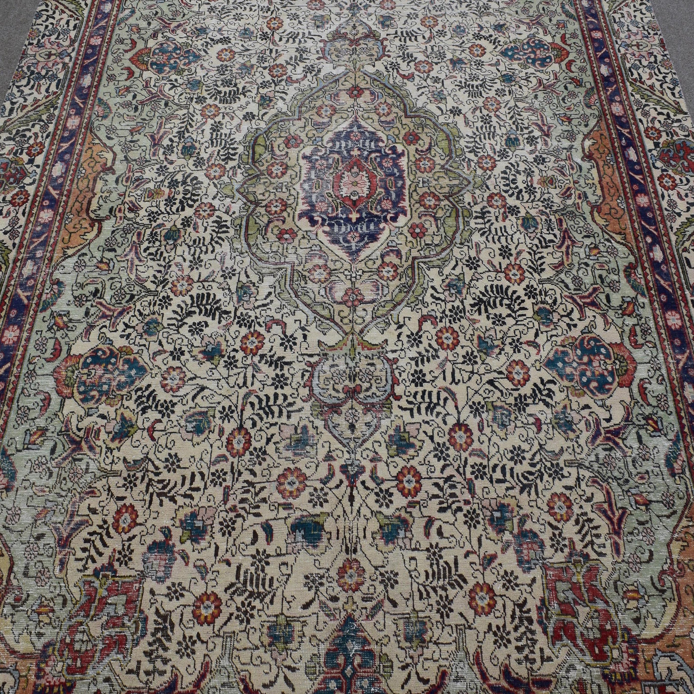 Close up of distressed Persian rug showing ornate medallion with colorful floral motifs