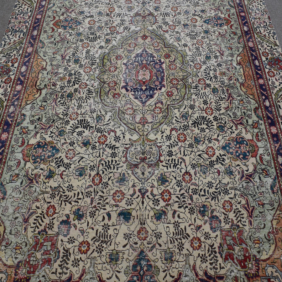 Close up of distressed Persian rug showing ornate medallion with colorful floral motifs