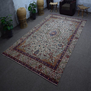 Hand knotted Persian rug photographed at an angle showing overall medallion layout and distressed ivory palette
