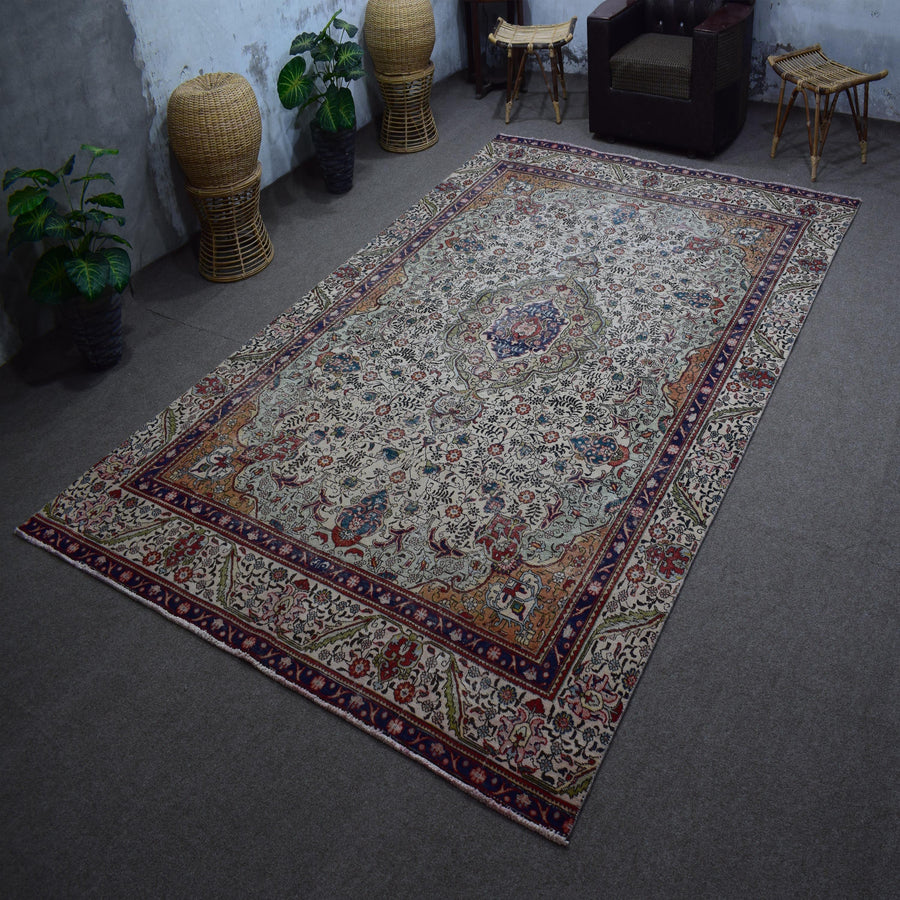 Hand knotted Persian rug photographed at an angle showing overall medallion layout and distressed ivory palette