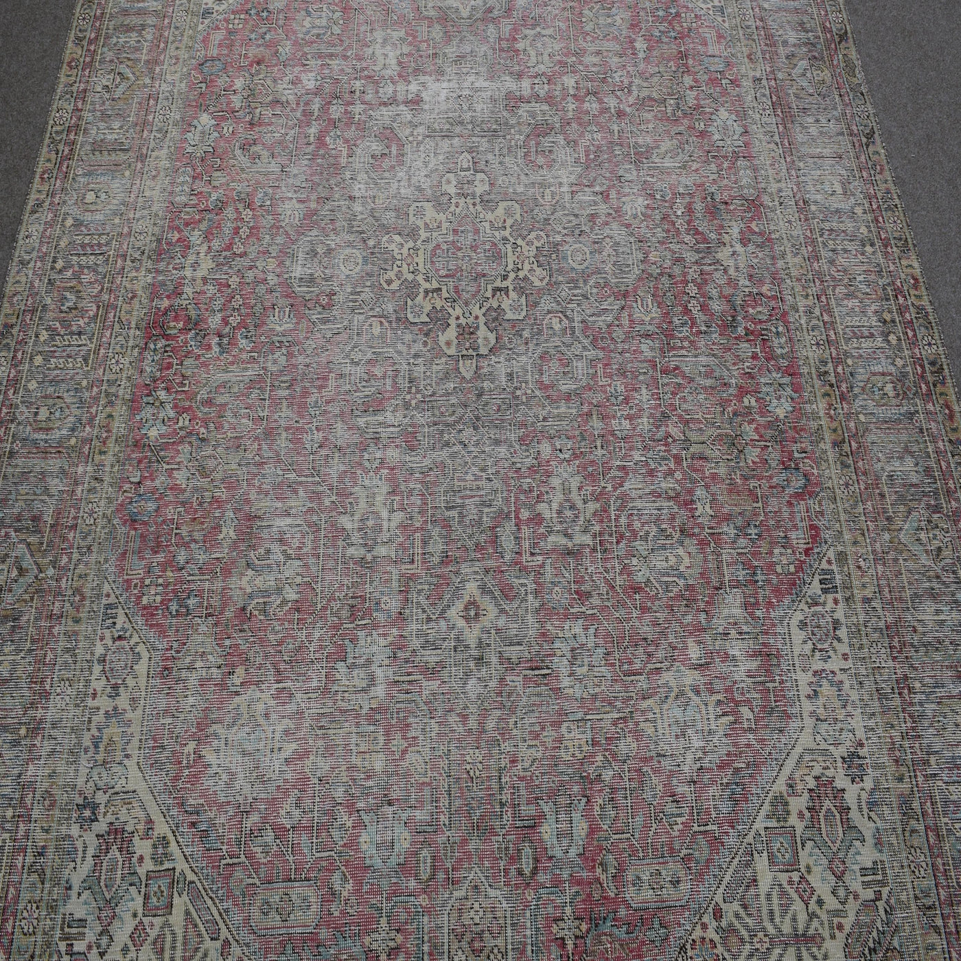Close up of distressed Persian rug showing faded floral motifs on rose background