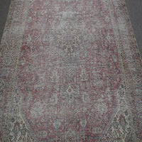 Close up of distressed Persian rug showing faded floral motifs on rose background