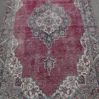 Close up of distressed Persian rug showing intricate floral medallion on faded red background