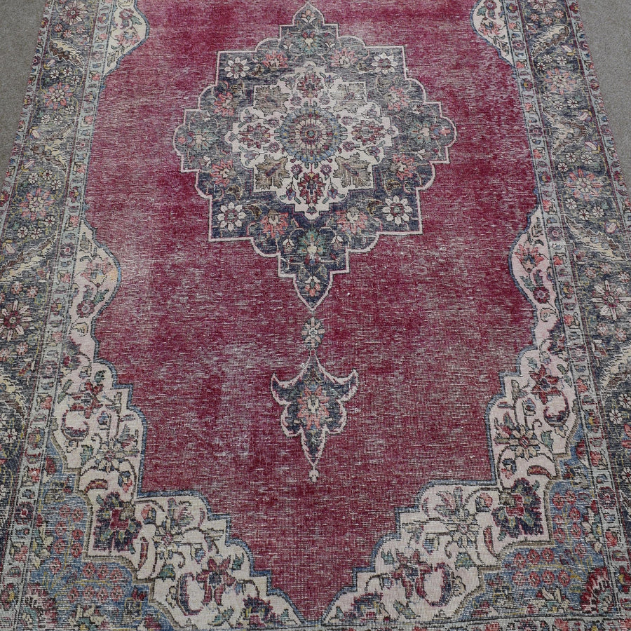 Close up of distressed Persian rug showing intricate floral medallion on faded red background
