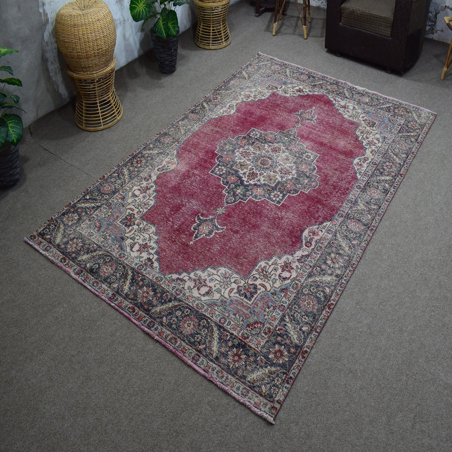 Hand knotted Persian rug photographed at an angle showing overall medallion layout and distressed red palette