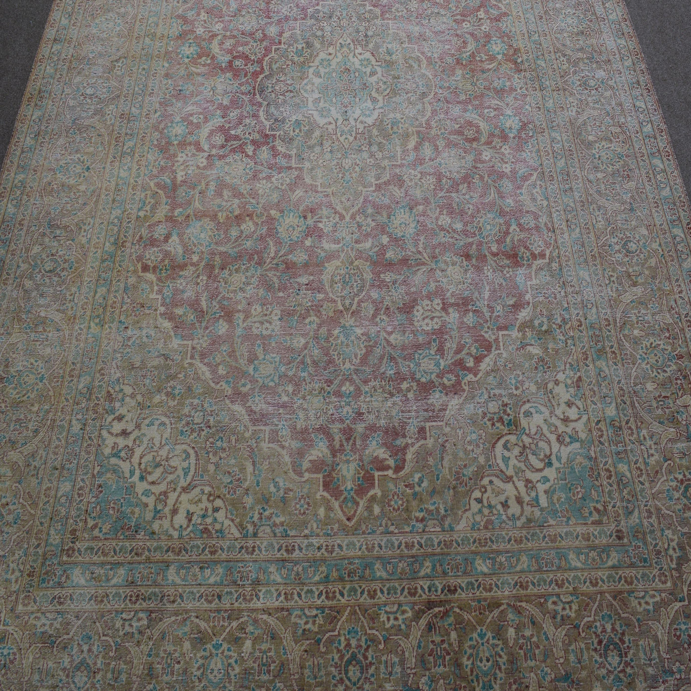 Close up of distressed Persian rug showing delicate floral motifs on faded ivory background