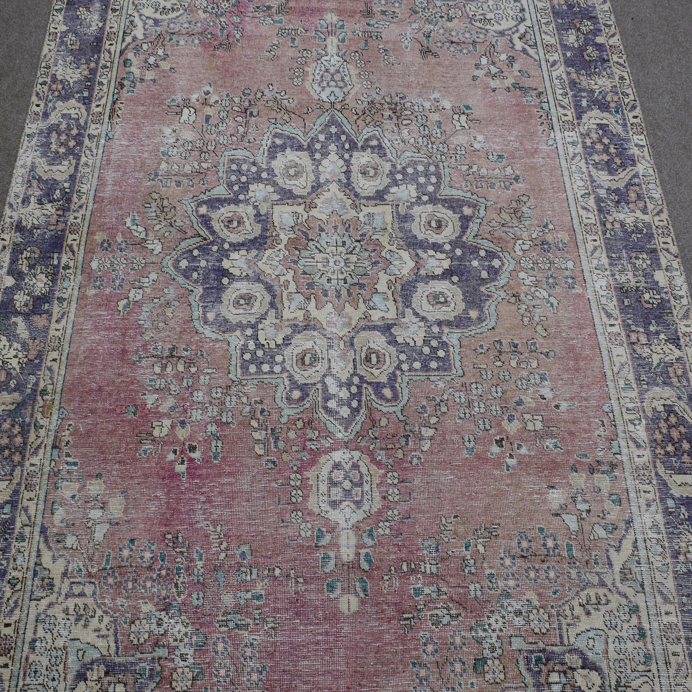 Close up of distressed Persian rug showing intricate floral medallion with blue and ivory motifs