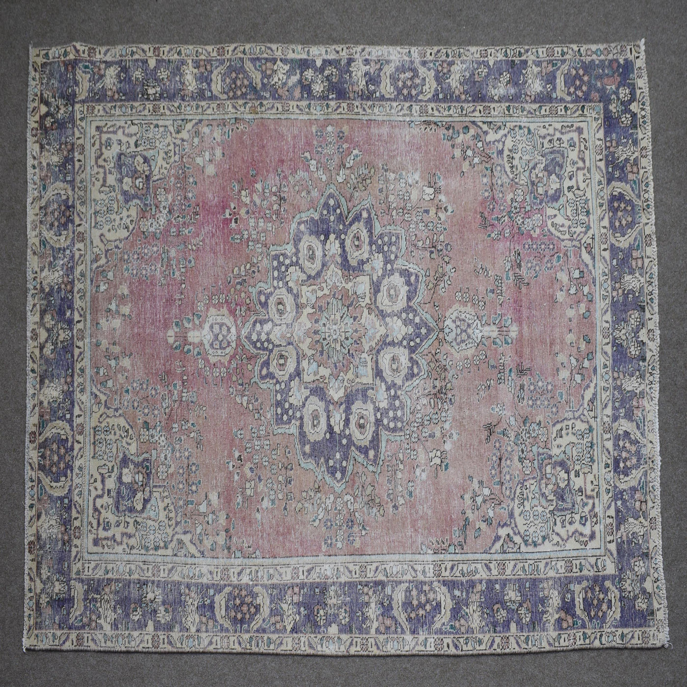 Hand knotted Persian rug photographed at an angle showing overall medallion layout and distressed rose tones