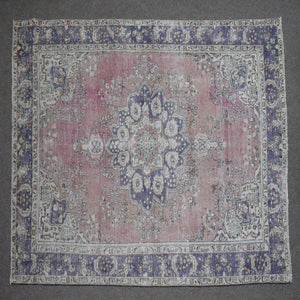 Hand knotted Persian rug photographed at an angle showing overall medallion layout and distressed rose tones