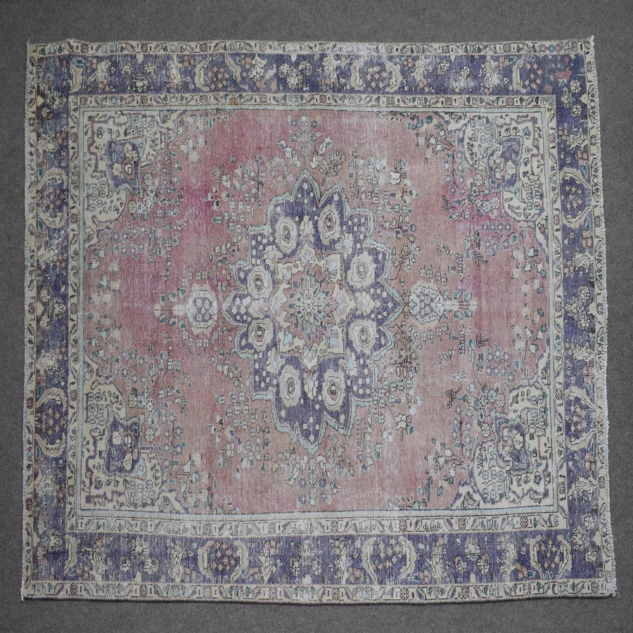 Hand knotted Persian rug photographed at an angle showing overall medallion layout and distressed rose tones