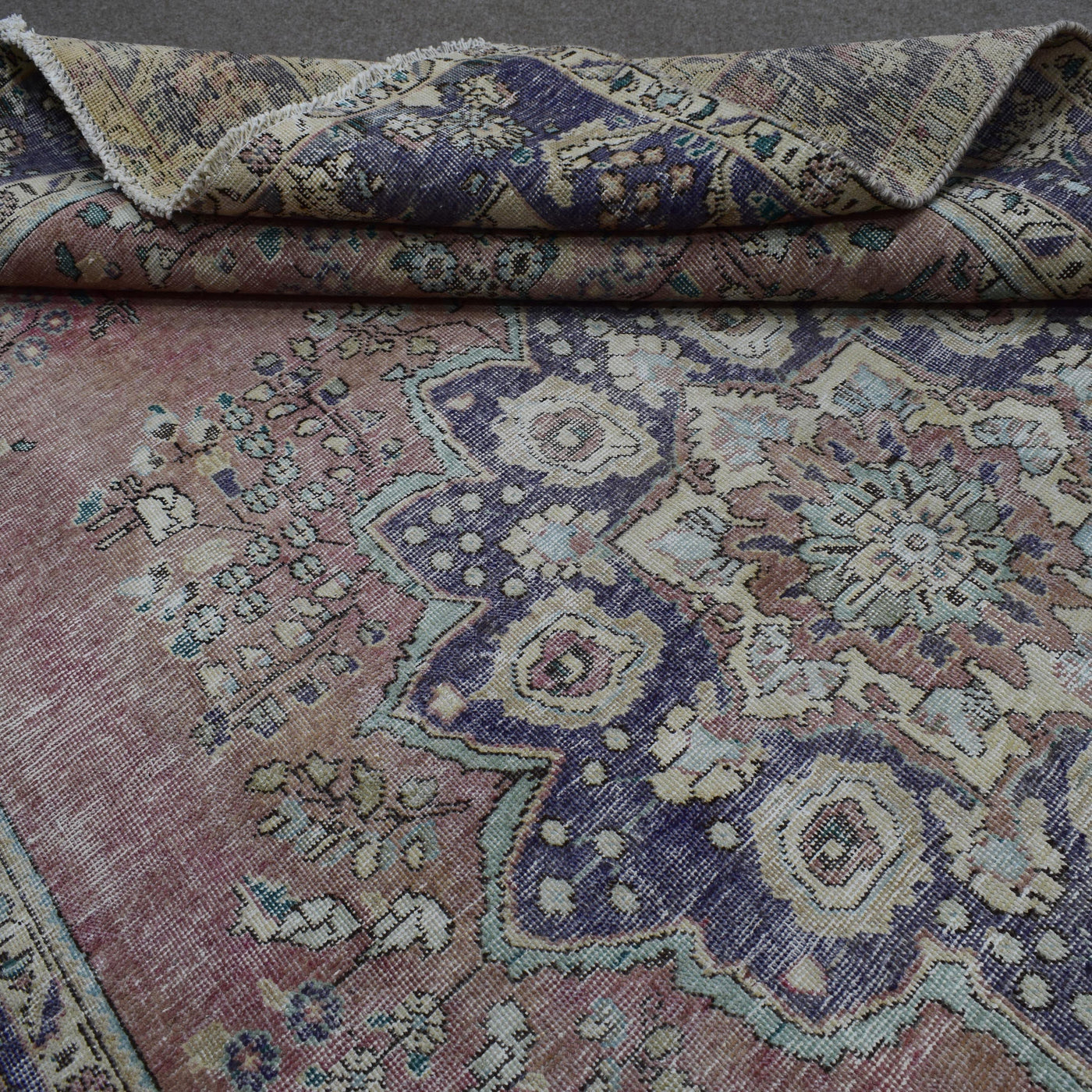 Detailed view of distressed Persian rug pattern with faded rose field and ornamental motifs