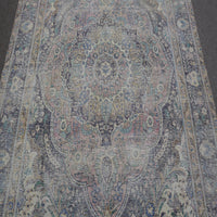 Close up of distressed Persian rug showing intricate floral medallion with blue and beige motifs