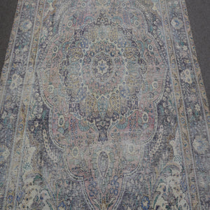 Close up of distressed Persian rug showing intricate floral medallion with blue and beige motifs