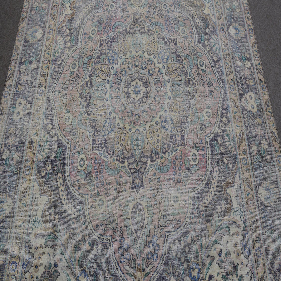 Close up of distressed Persian rug showing intricate floral medallion with blue and beige motifs