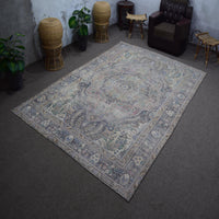 Hand knotted Persian rug photographed at an angle showing overall medallion layout and distressed neutral palette