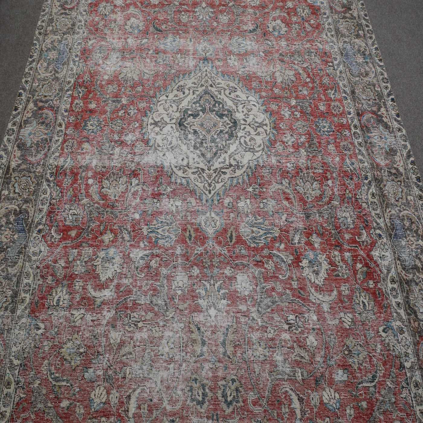Close up of distressed Persian rug showing intricate floral medallion on faded red background