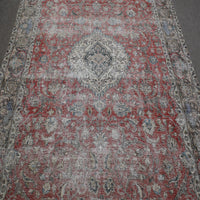 Close up of distressed Persian rug showing intricate floral medallion on faded red background