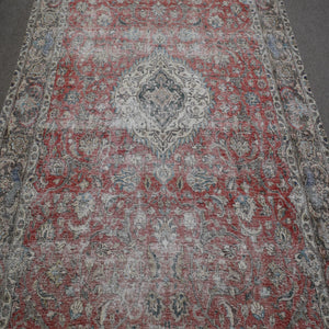 Close up of distressed Persian rug showing intricate floral medallion on faded red background
