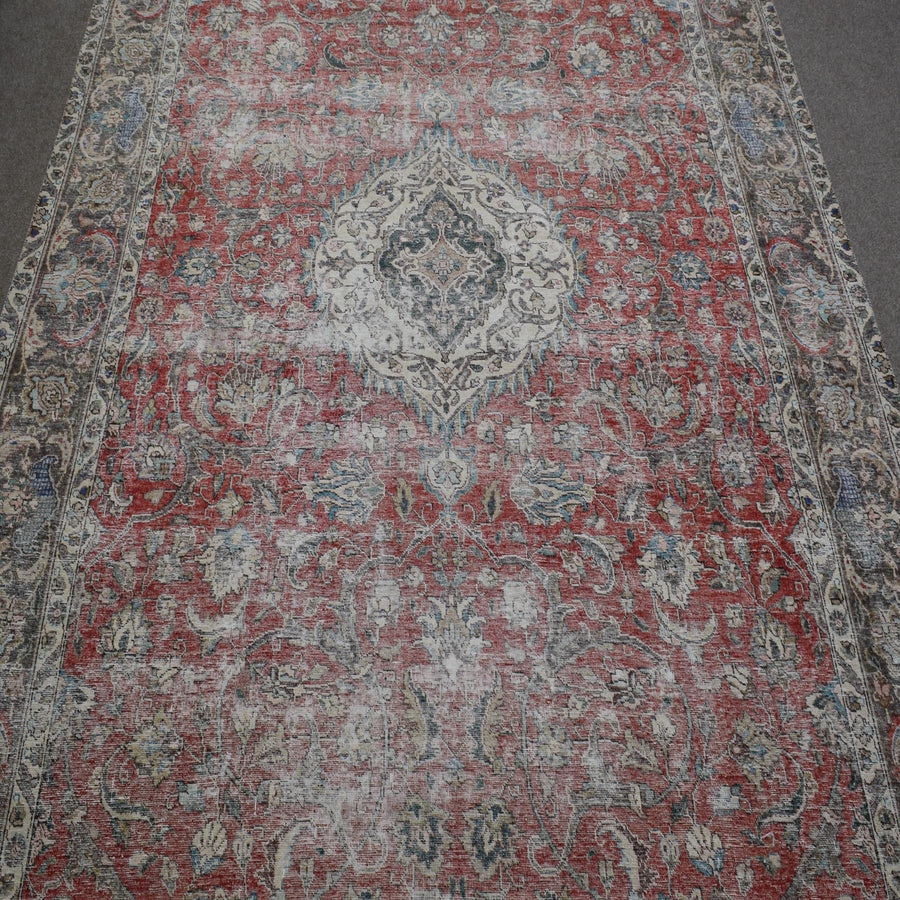 Close up of distressed Persian rug showing intricate floral medallion on faded red background