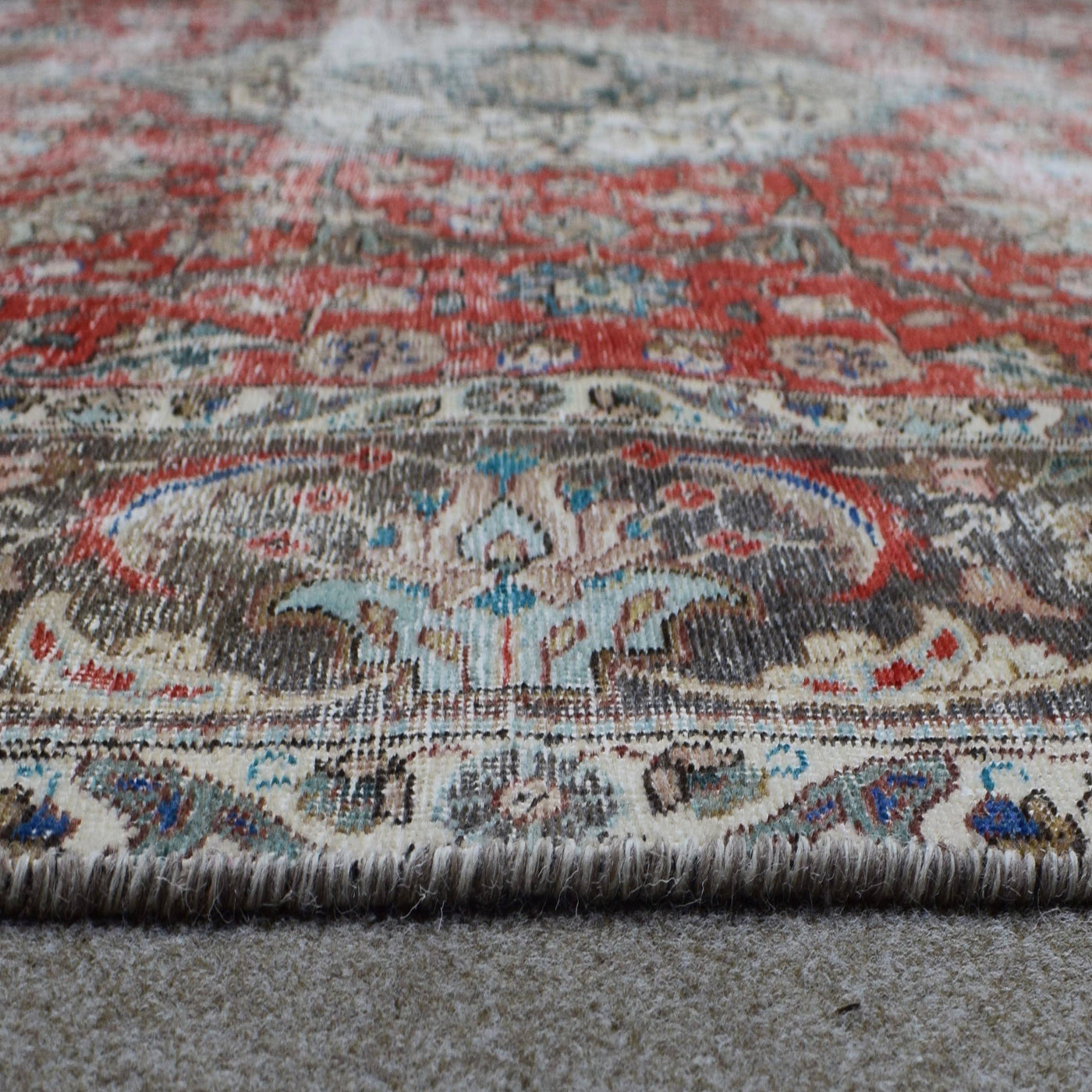 Hand knotted Persian rug photographed at an angle showing overall medallion layout and distressed vintage palette